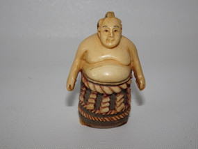 Japanese carved ivory netsuke of a sumo wrestler wearing an elaborate ceremonial kesho-mawashi, signed