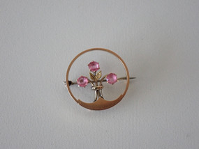 Antique 9ct gold circle brooch with three round faceted pink gemstones arranged as flowers, textured gold leaves and slender stems.