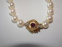 Vintage cultured pearl necklace and bracelet with 14 carat gold clasp set with a central ruby and diamonds displayed on a light background.