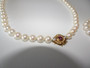 Vintage cultured pearl necklace and bracelet with 14 carat gold clasp set with a central ruby and diamonds displayed on a light background.