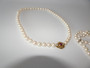 Vintage cultured pearl necklace and bracelet with 14 carat gold clasp set with a central ruby and diamonds displayed on a light background.