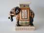 Vintage Hollywood Regency style Chinese ceramic elephant plant stand with glossy black glaze, ornate ceremonial saddle and colourful relief decoration.
