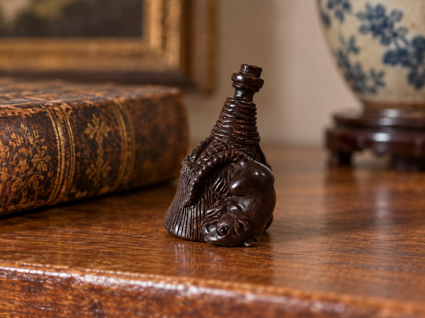Antique Japanese carved wood rat and hand-broom netsuke displayed on a wooden shelf beside an antique book