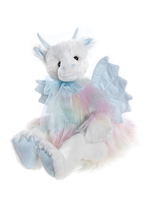 A white plush dragon teddy bear sits upright, featuring rainbow-coloured fur, blue horns, wings, claws, and a light blue satin bow tied around its neck.