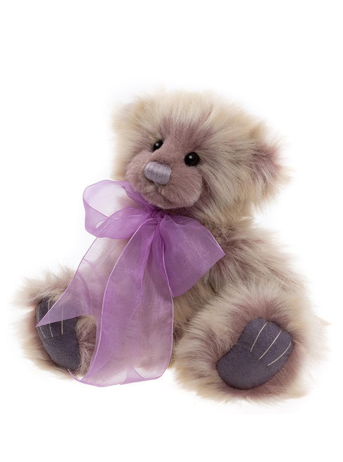 A plush Charlie Bear teddy bear in cream and mauve tones sits upright against a white background, wearing a sheer purple organza ribbon bow around its neck.