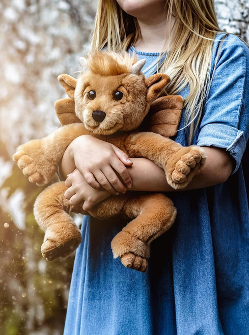 A tan/golden dragon-styled teddy bear sits upright, featuring wings, small horns, pointed ears, and large clawed feet, photographed against a white background.