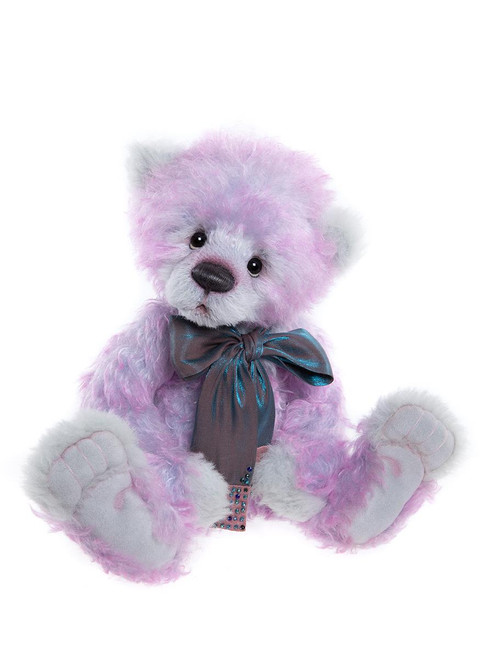 A pink and white fluffy teddy bear sits upright, wearing a shimmery teal and grey bow tie with a rhinestone embellishment, against a white background.