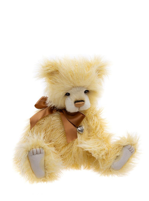 A pale yellow fluffy teddy bear sits upright against a white background, wearing a bronze satin bow tie with a small silver heart charm.