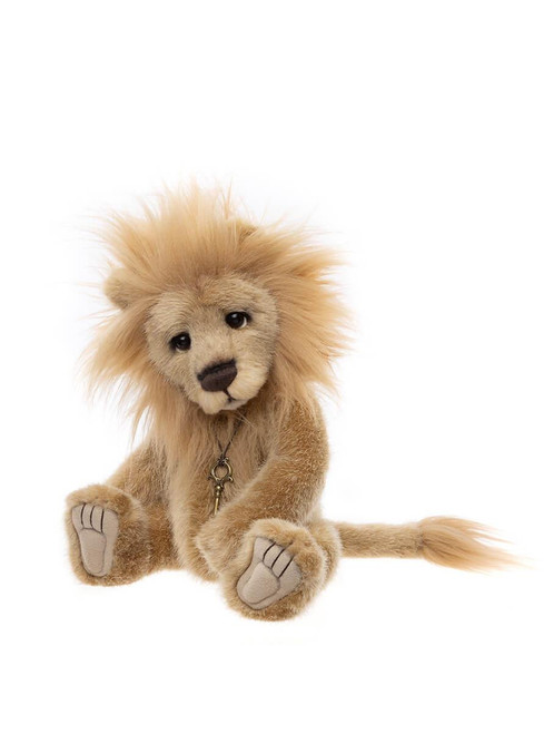 A plush lion teddy bear sits upright against a white background, featuring a fluffy golden mane, suede paw pads, and a small antique key pendant necklace.