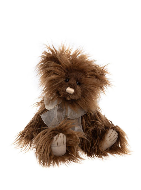 A shaggy, long-haired brown teddy bear sits upright against a white background, wearing a sheer silver ribbon bow, with cream-colored paw pads visible on its feet and hands.