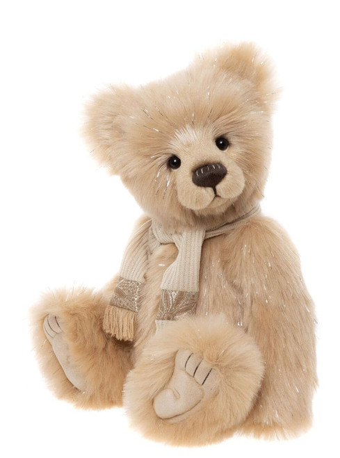 A plush cream-coloured teddy bear sits upright wearing a knitted cream and gold scarf with fringe detail. The bear features subtle silver tinsel highlights throughout its fur.
