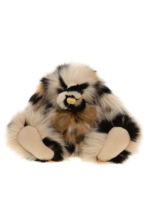 A fluffy Charlie Bears teddy bear with cream and black patchy fur sits upright, wearing a gold organza bow, with large flat paws extended forward, against a white background.