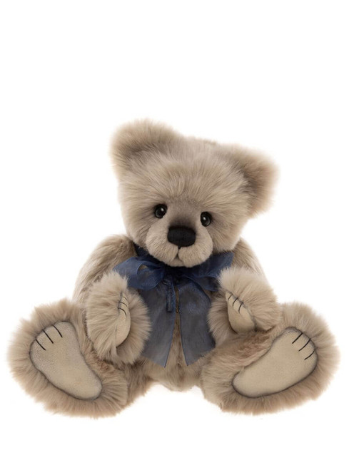 A plush, beige teddy bear sits upright against a white background, wearing a blue ribbon bow at its neck, with large paws and small black eyes.