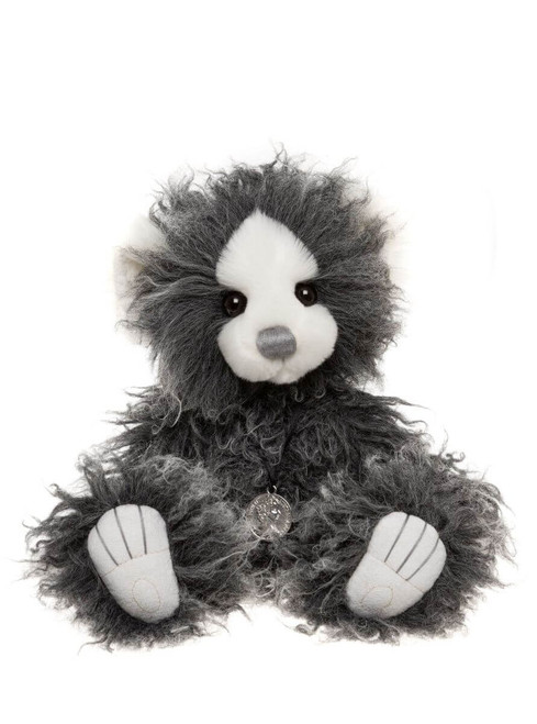 A grey and white curly-furred Charlie Bears teddy bear sits upright against a white background, featuring black eyes, white muzzle, pale paw pads, and a small silver medallion pendant.