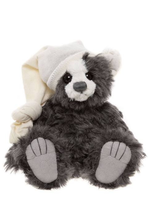 A grey and white fluffy Charlie Bears teddy bear sits upright, wearing a cream knitted nightcap and matching mittens, with grey paw pads visible on outstretched feet.