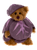 A brown Charlie Bears teddy bear sits wearing a purple plush eggplant/aubergine costume, complete with a matching rounded body suit and cap, against a white background.