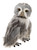 A grey and white plush owl teddy bear stands upright, facing forward, with amber eyes, striped feather detail, and black taloned feet, against a white background.