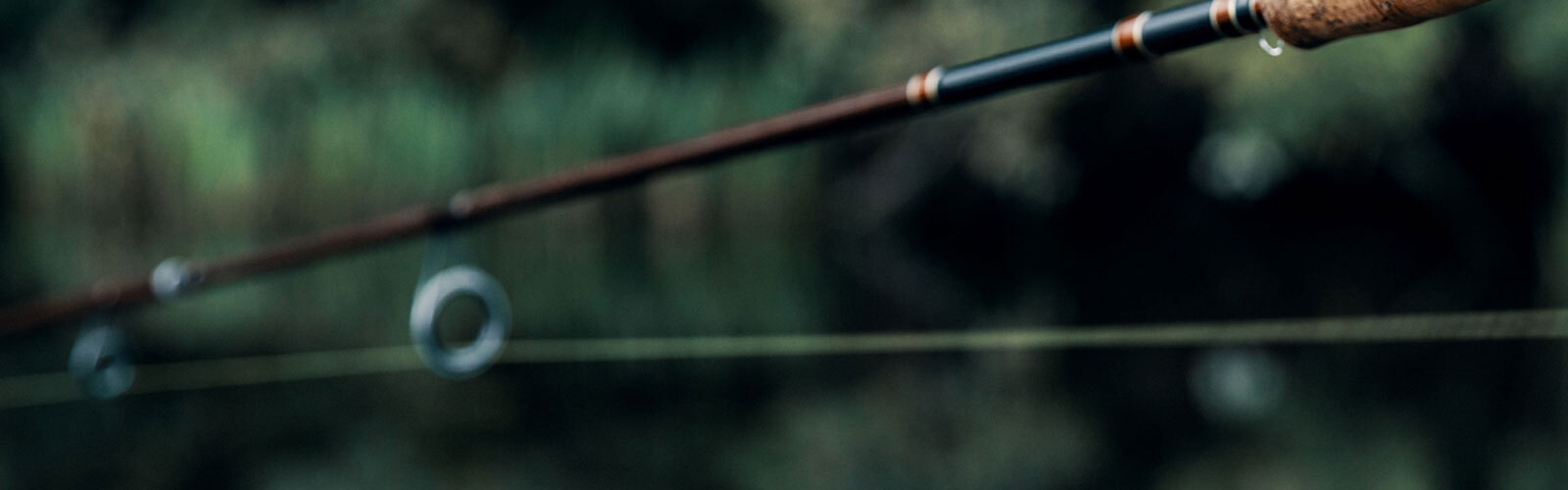 Close-up fishing rod with blurred green water background, calm mood highlighting fine craftsmanship.
