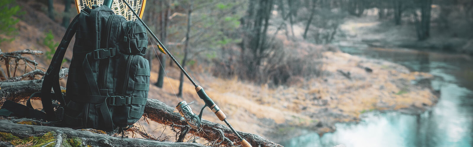 A black backpack, fishing rod, and net sit on a log by a calm river, with soft, muted forest tones.
