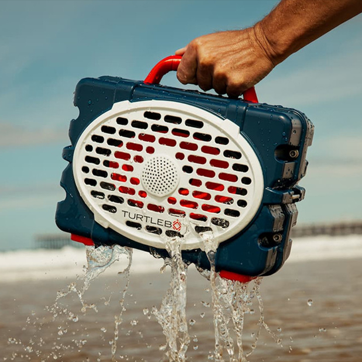 A lifestyle image of a person holding a Tutrlebox speaker on the beach with water pouringout