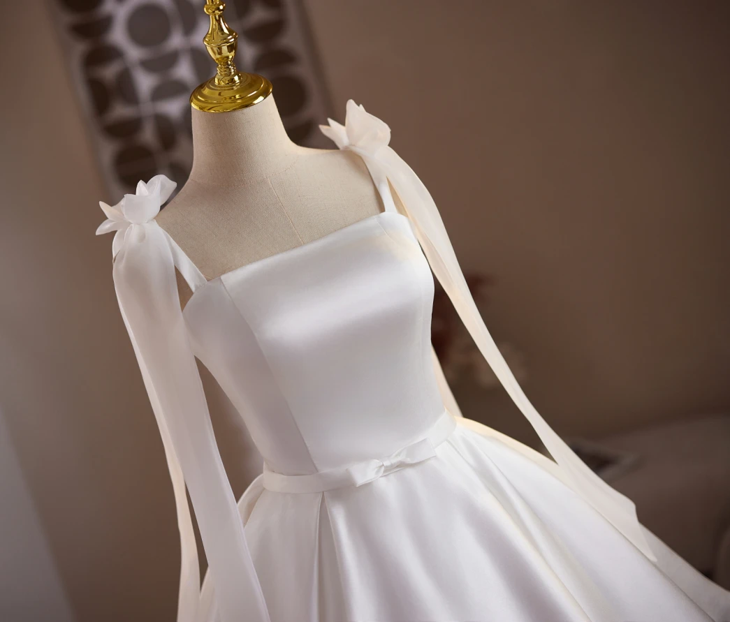 White satin short homecoming dress with flower shoulder straps, ribbon streamers, square neckline and pleated A-line skirt