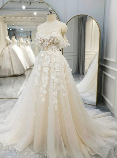 Romantic off-the-shoulder bohemian wedding dress with floral lace appliqués and flowing tulle skirt.