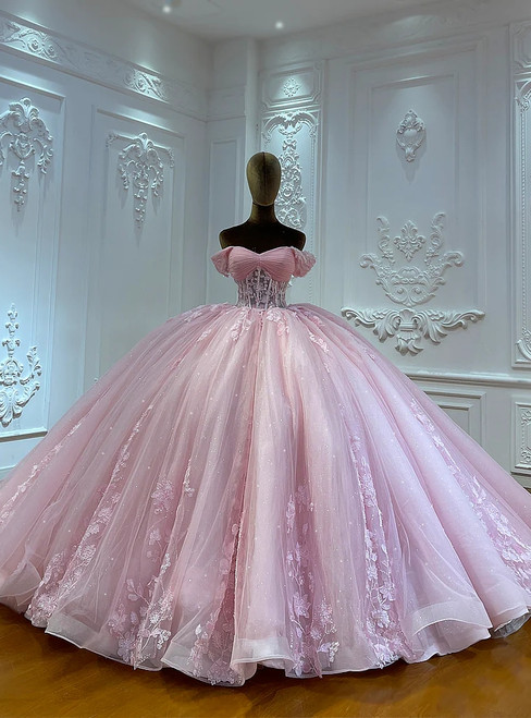 A petal pink tulle ball gown, its off-shoulder bodice adorned with delicate appliqués and soft, sculpted pleats that create a silhouette of organic, flowing beauty.