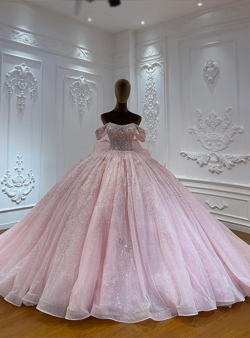 A rosy champagne tulle ball gown, its off-shoulder bodice shimmering with scattered sequins that create a soft, luminous aura like the first light of dawn.