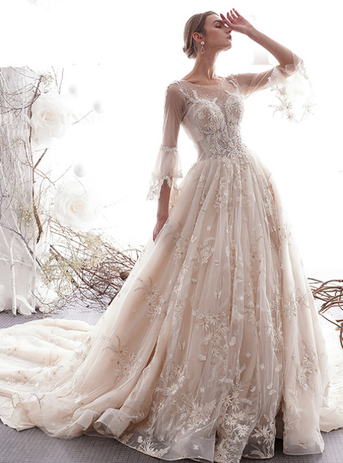 Champagne ball gown wedding dress with a full tulle skirt, 3/4 sheer sleeves, intricate lace appliqués, and a long, dramatic train.