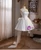 Back view of a white satin homecoming dress featuring a lace-up closure and a sleek, minimalist silhouette.