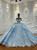 An ocean queen blue ball gown, its off-shoulder bodice a masterpiece of lace, sequins, and beaded appliqués that shimmer like light through deep sea water.