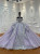 A lavender tulle ball gown, its off-shoulder bodice adorned with beaded floral appliqués that gleam softly like dewdrops on petals at twilight.