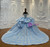The layered blue tulle skirt creates a full, flowing volume, its surface adorned with delicate appliqués that gleam with a cool, crystalline beauty.