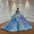 Floral lace appliques gently trace the off-shoulder neckline, giving this blue tulle gown a soft, romantic front view that contrasts with its dramatic back.