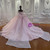 Back view of a pink wedding dress showcasing a beautiful large bow at the waist, a lace-up corset back, and a sweeping tulle train.