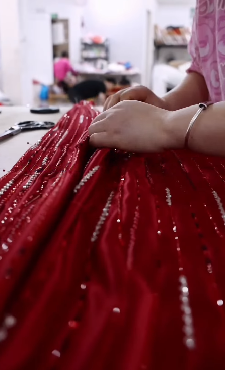 Artisan hand stitching diagonal bead rows onto a flat red satin dress panel
