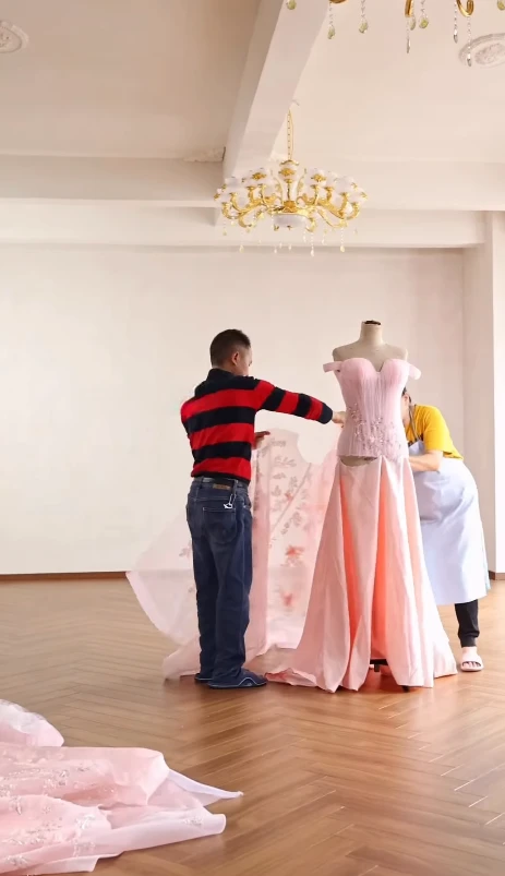 Artisans spreading a sparkling lace train for a custom pink couture gown