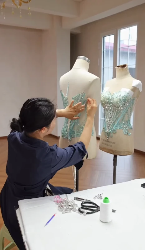 Atelier artisan hand beading the bodice of a mint green crystal ball gown