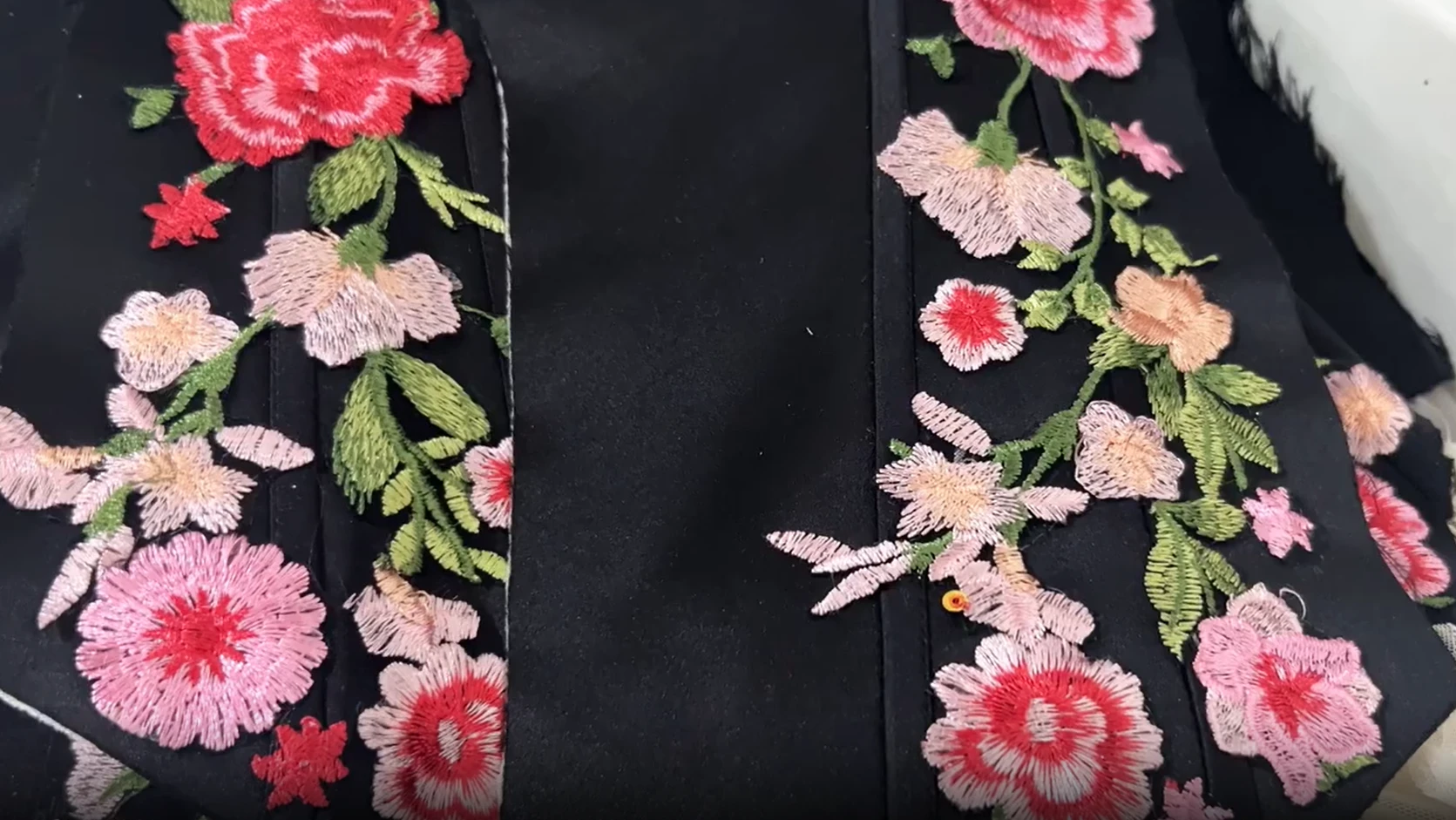 Close up of hand embroidered pink and red roses on black fabric