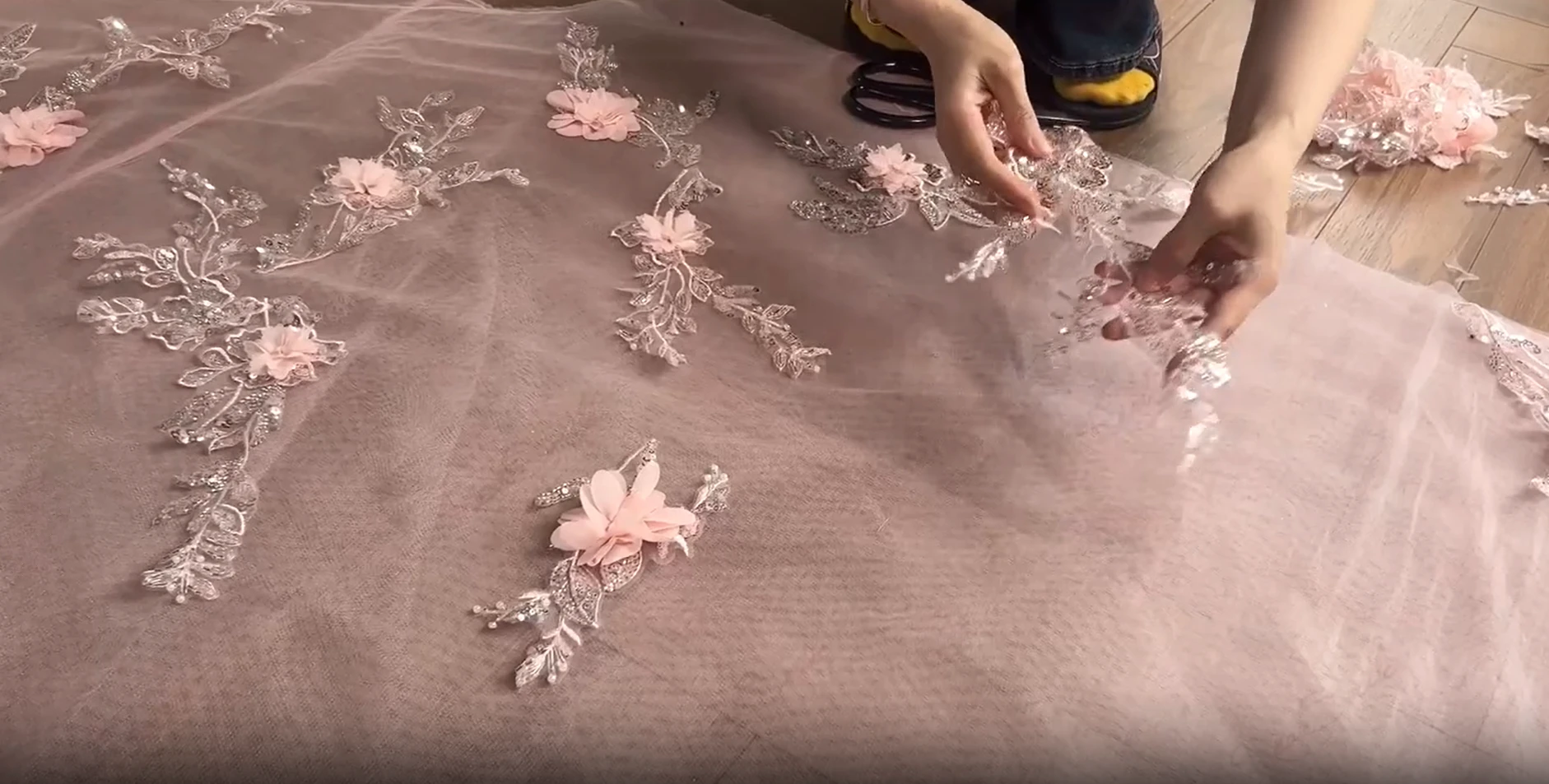 Craftsman arranging floral lace patches on soft pink tulle for a luxury prom dress
