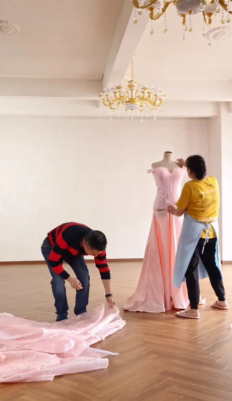 Craftsmen arranging lace and tulle fabric for a luxury pink formal gown