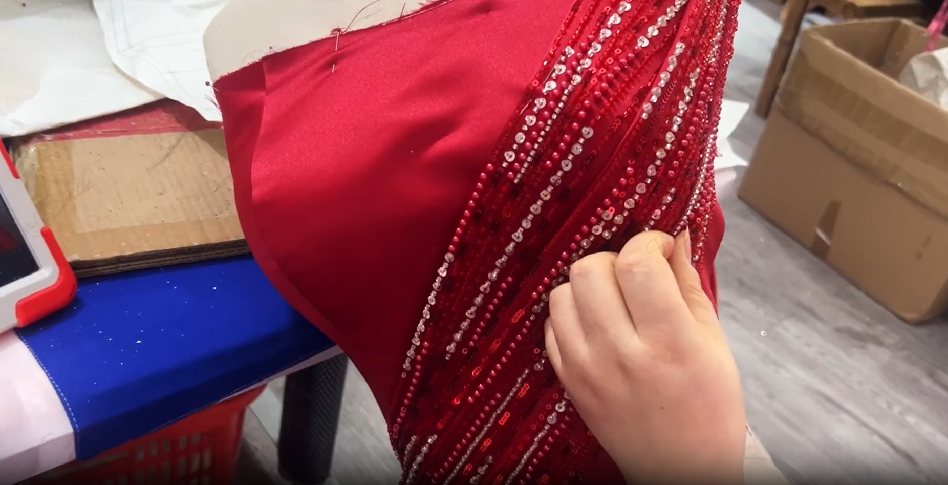 Dressmaker tucking beaded red satin pleats into position on a mannequin