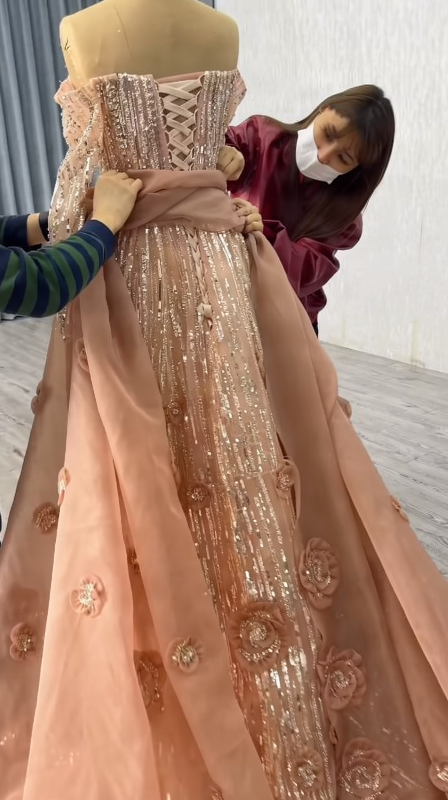 Fitters performing the final adjustment on the champagne pink prom dress with long sleeves and floral embellishments