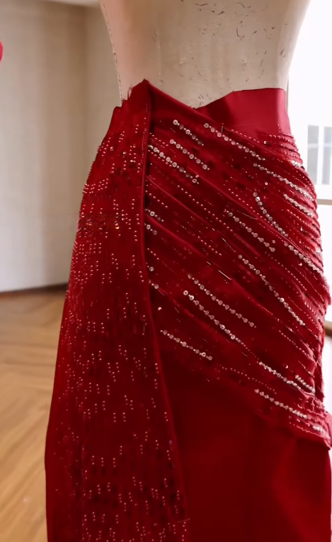 Hand-beaded diagonal satin pleats shaped around the waist of a red gown on a dress form