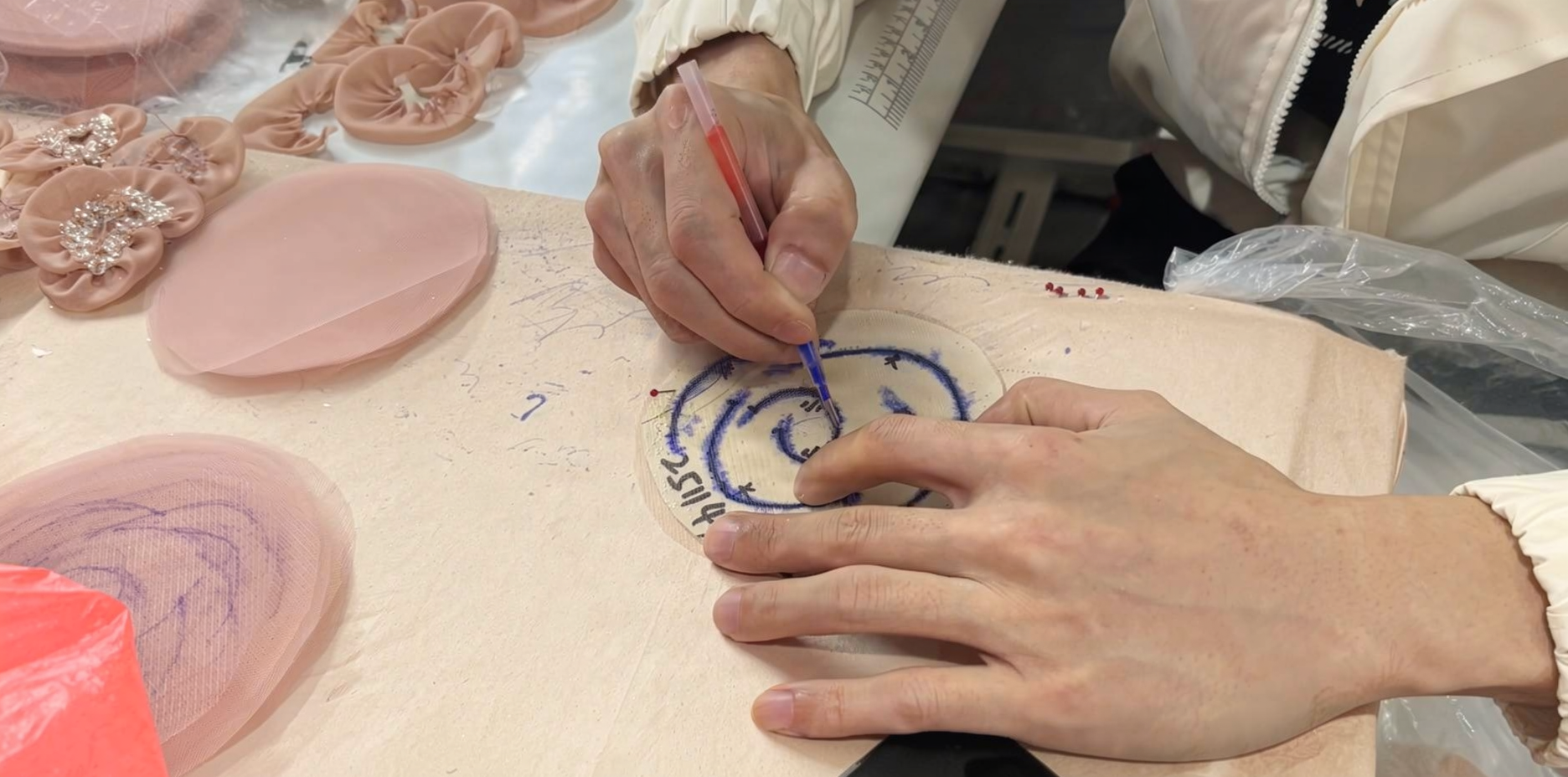 Couturier tracing the floral motif pattern onto the champagne pink tulle, preparing for the hand-embellishment process