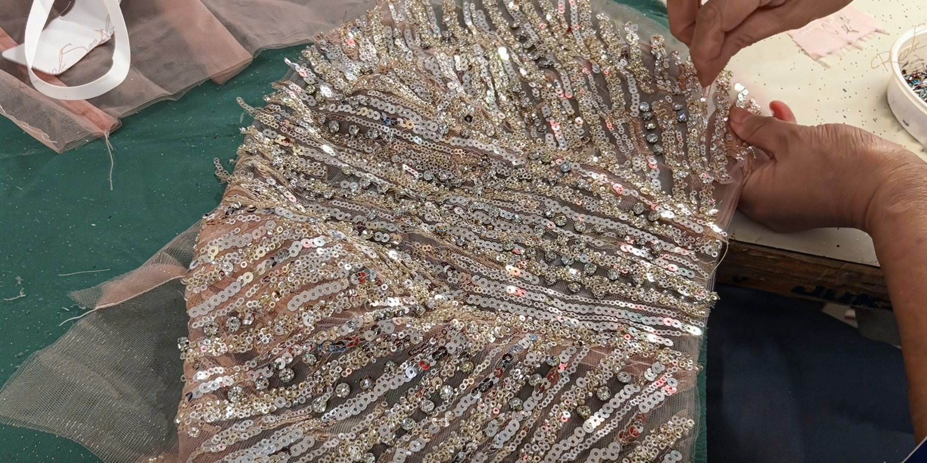 Hands arranging the champagne pink fabric with intricate sequin and fringe trim detail on the atelier work table