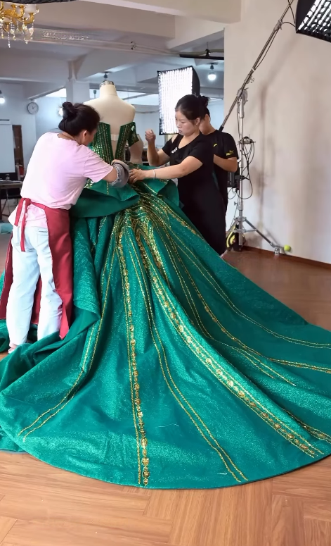 Tailor adjusting ornate emerald gown train