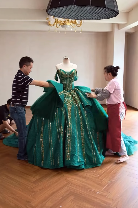 Workers positioning voluminous emerald ball gown