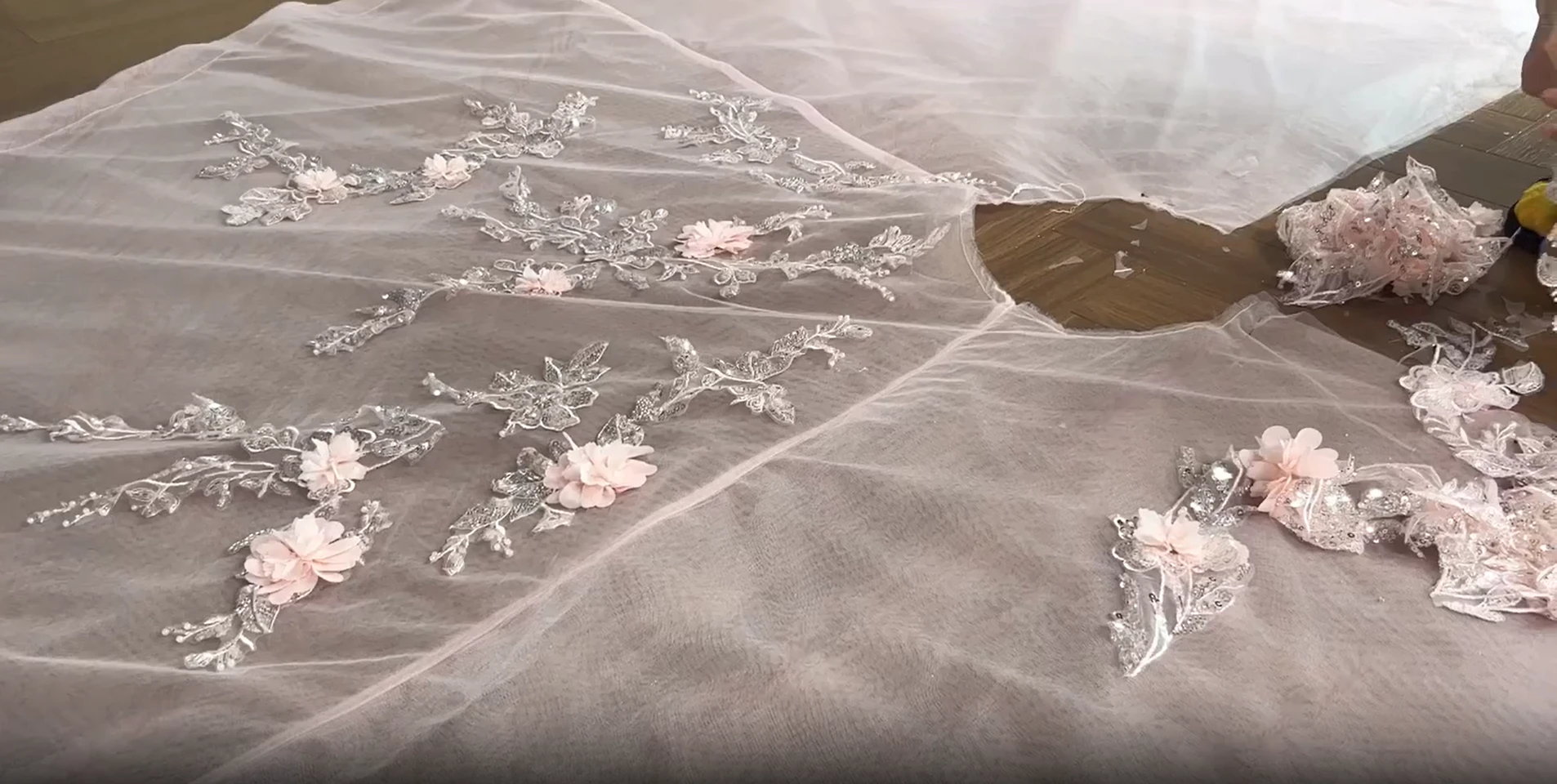 Dressmaker placing three dimensional floral appliques onto sheer tulle gown fabric