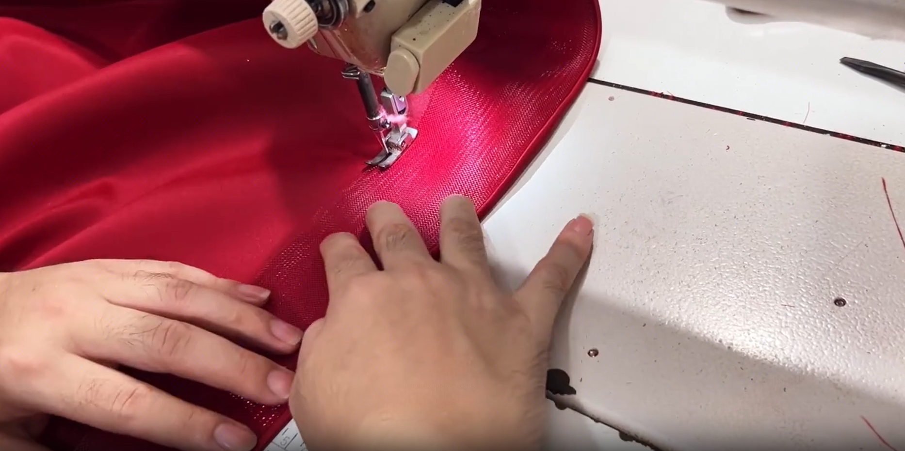 Tailor sewing crinoline support into the satin edge of a red formal gown